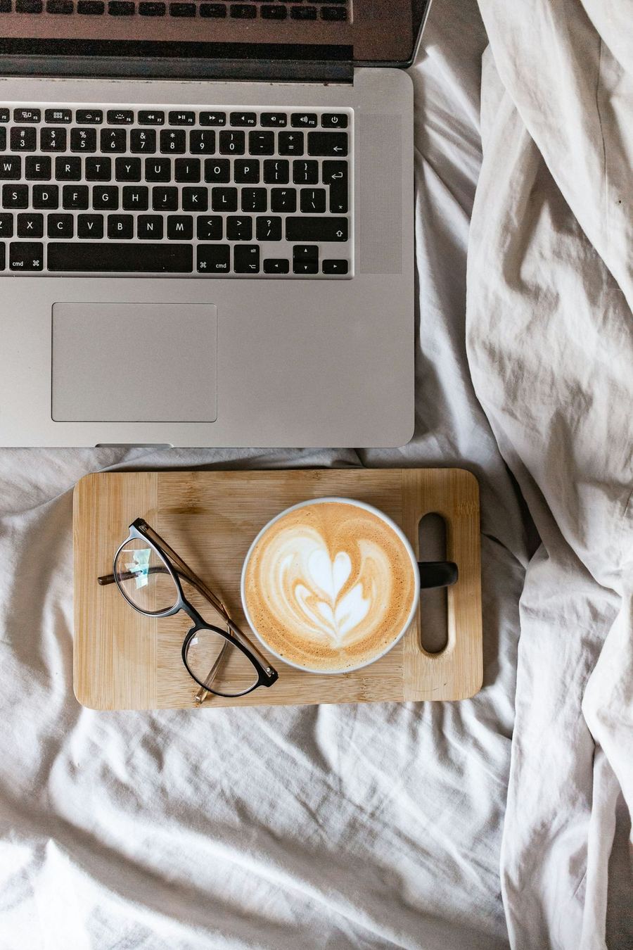 A laptop, latte, and glasses on soft white linen